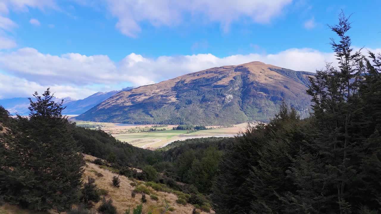 Panoramic view of Glenorchy's mountainous landscape with lush greenery under bright daylight and clear skies