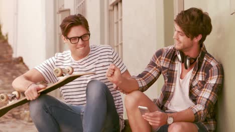 smiling hipster friends sitting together while holding skateboard