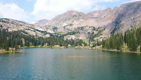 aerial drone flies low near clear blue lake water then rises towards beautiful mountain peak and pine tree forest in nederland colorado during summer in the rocky mountains