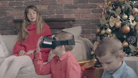 madre sentada en el sofá observa a sus hijos jugando con regalos