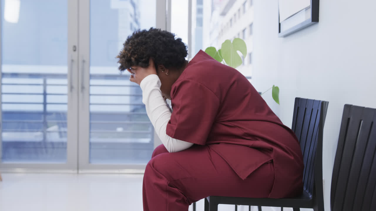Tired african american female doctor sitting in hospital waiting room, slow motion