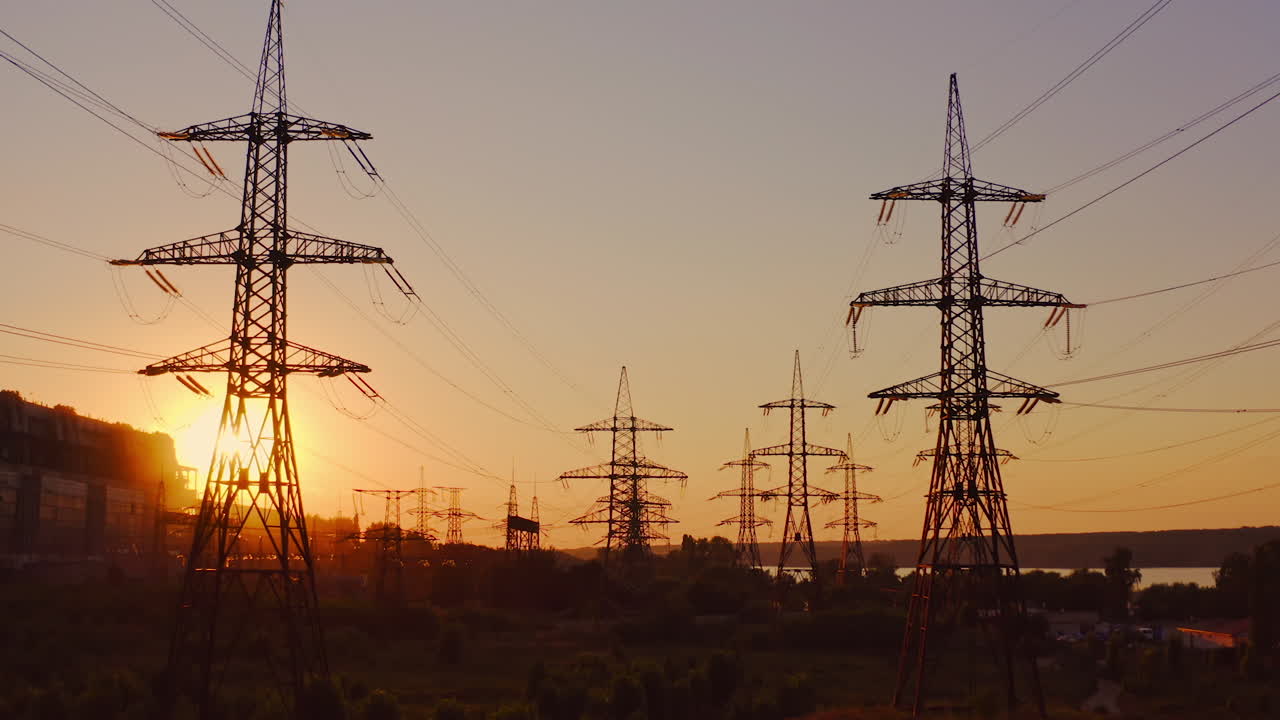 High-voltage power towers. The dark silhouette of towers in the rays of the beautiful evening sun. Electric pylons at dusk. Global warming.