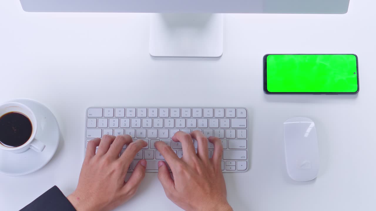 Top view of businessman typing on white keyboard at workdesk with green screen smartphone and coffee