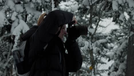mujer joven en ropa de invierno sosteniendo una cámara digital tomando fotografías en un paisaje natural nevado en el parque nacional mont chauve, orford, quebec, canadá