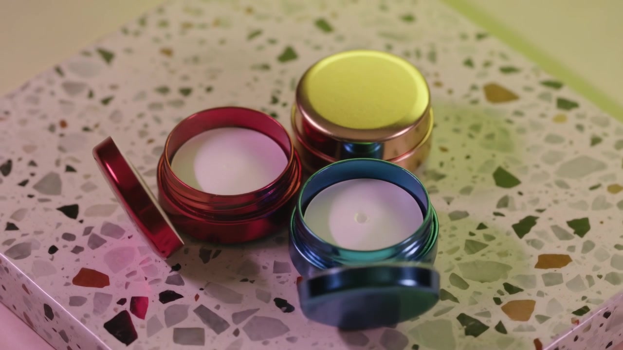 Opening off-camera hand lifting lids from three metal tins on terrazzo slab, revealing wax