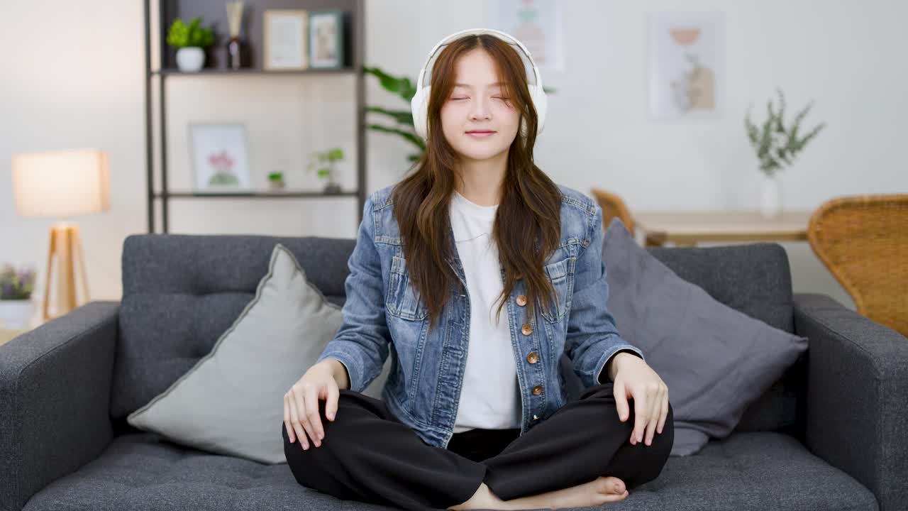 A young woman puts on headphones and meditates with eyes closed in a bright room