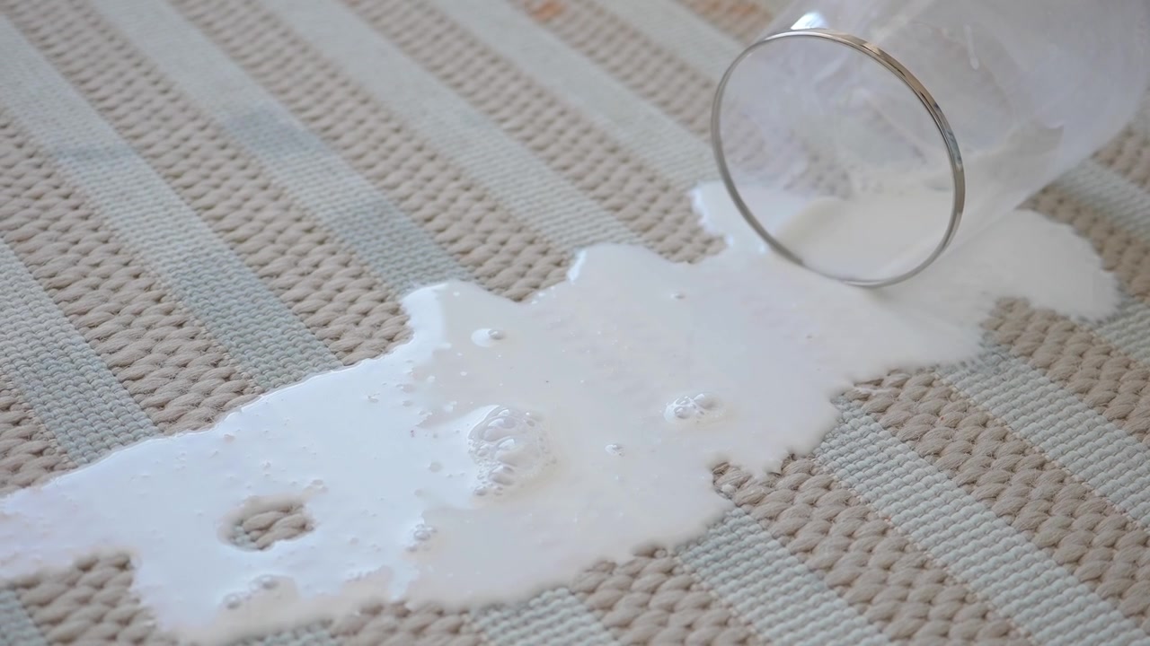 Latte che si rovescia da un bicchiere su un tappeto a righe