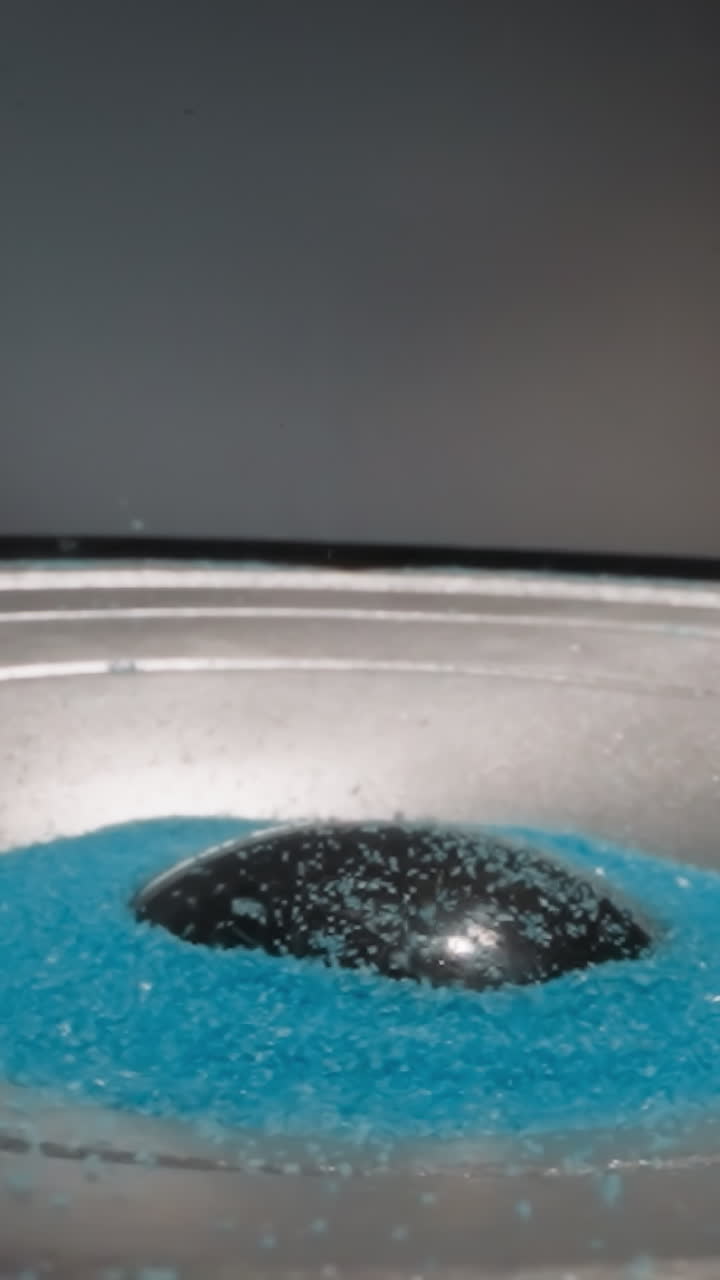 Loudspeaker plays music and throws blue hydrophobic sand upward. Colored aquarium sand moves depending on intensity of sound waves. Demonstration of acoustic system operation macro