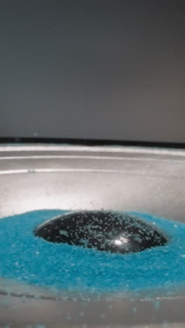 loudspeaker plays music and throws blue hydrophobic sand upward. colored aquarium sand moves depending on intensity of sound waves. demonstration of acoustic system operation macro