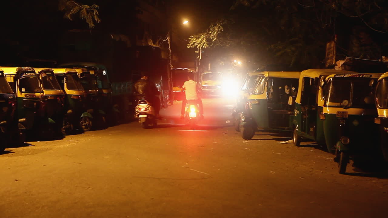 Auto rickshaws parked on a quiet street at night in Bangalore lit by streetlights and vehicle headlights