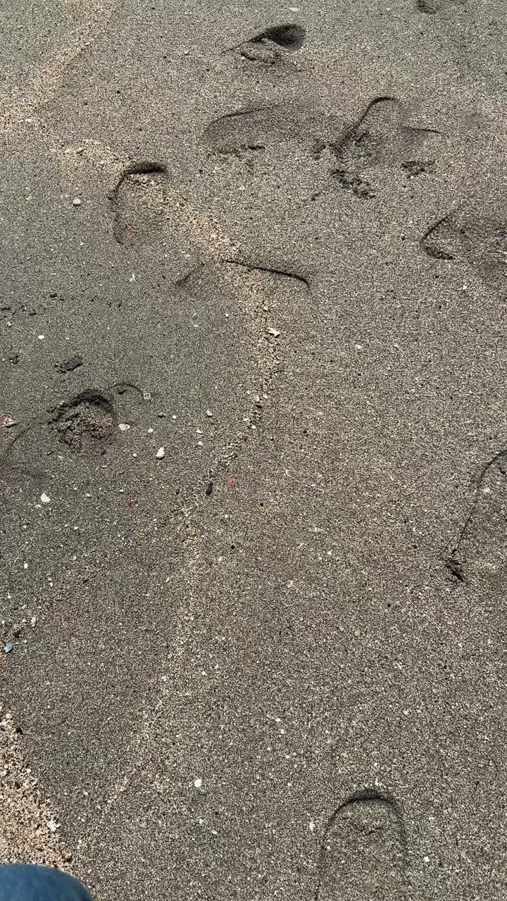 Vista in prima persona di impronte su una spiaggia di sabbia scura