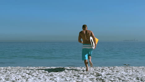 hombre guapo con una tabla de surf corriendo hacia el mar