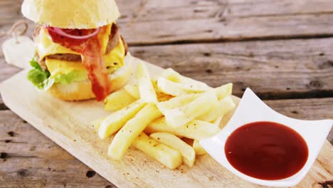 hamburger and french fries with tomato sauce kept on chopping board