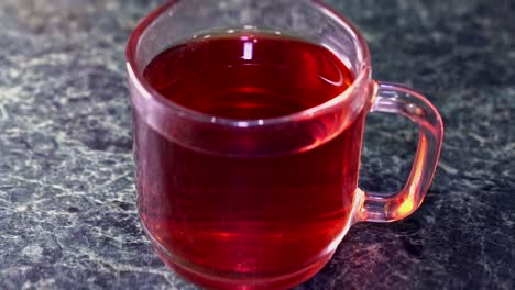 sugar is poured into a glass cup of tea and stirred