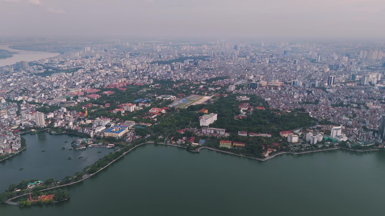 Aerial view of Hanoi, Vietnam, showing West Lake Tay Ho and the sprawling cityscape with dense urban housing, greenery, and modern skyline at dusk. UHD