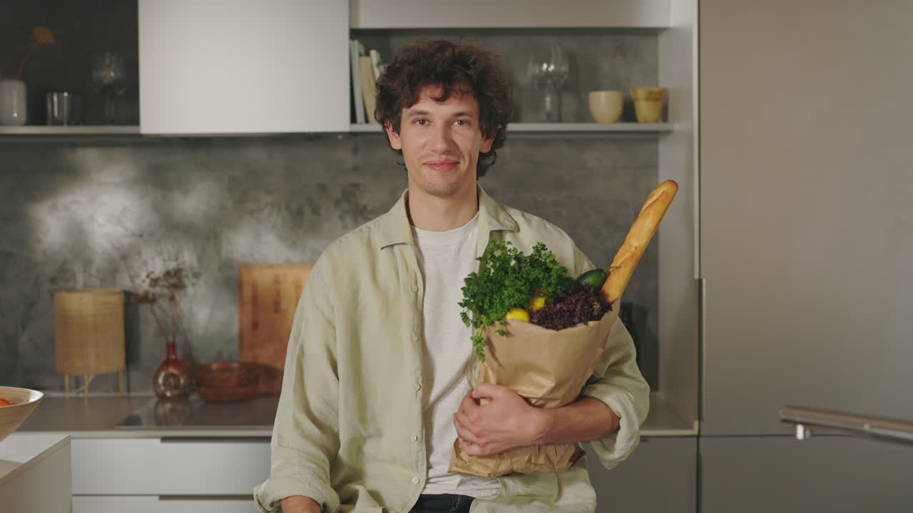 A young man holding a bag of groceries in a modern kitchen