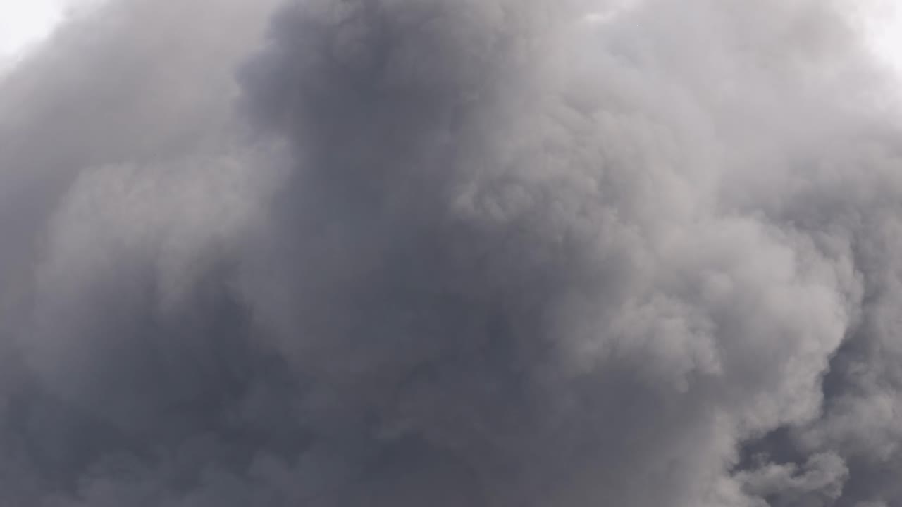 Thick, dark smoke clouds billow intensely, filling the frame with dynamic movement and dramatic atmosphere