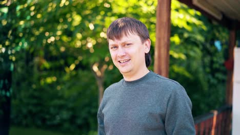 close-up portrait young man stands on the background of a summer house and greenery and smiles