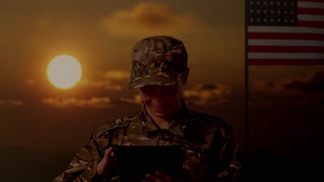 close up of asian man soldier using a tablet while standing with flag of the united states, sunset time