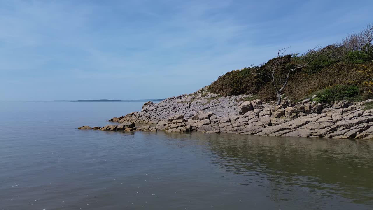 Aerial view circling weathered rocky coastal slope and lush idyllic wilderness with mountain horizon