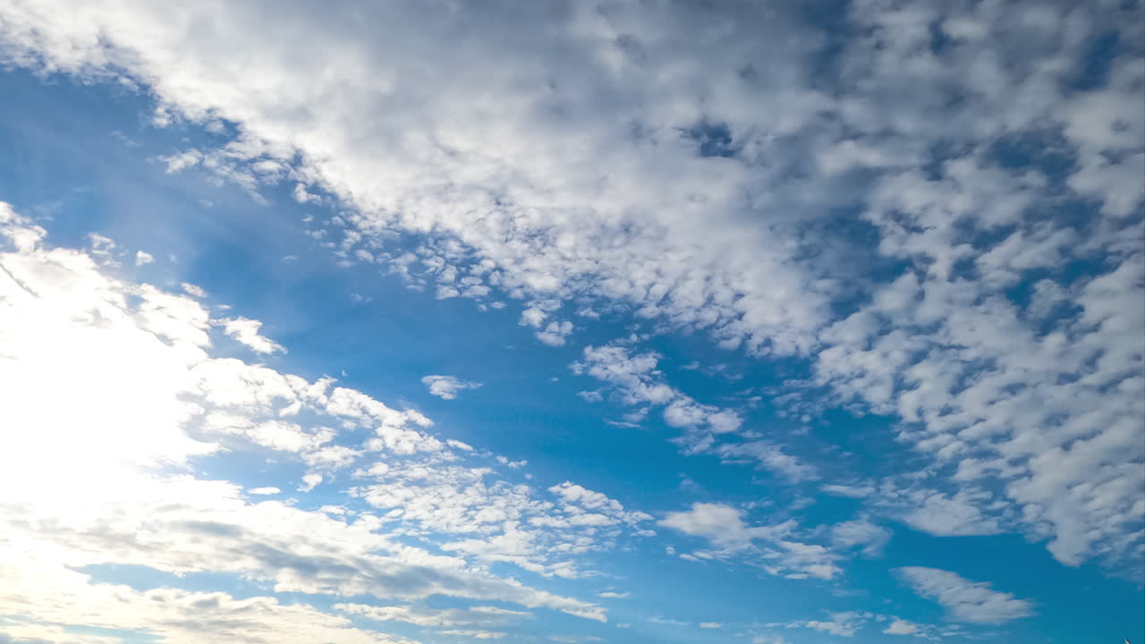 Beautiful light spindrift clouds fly away opening blue skies. Sun rays coming through the clouds. Timelapse view from below.