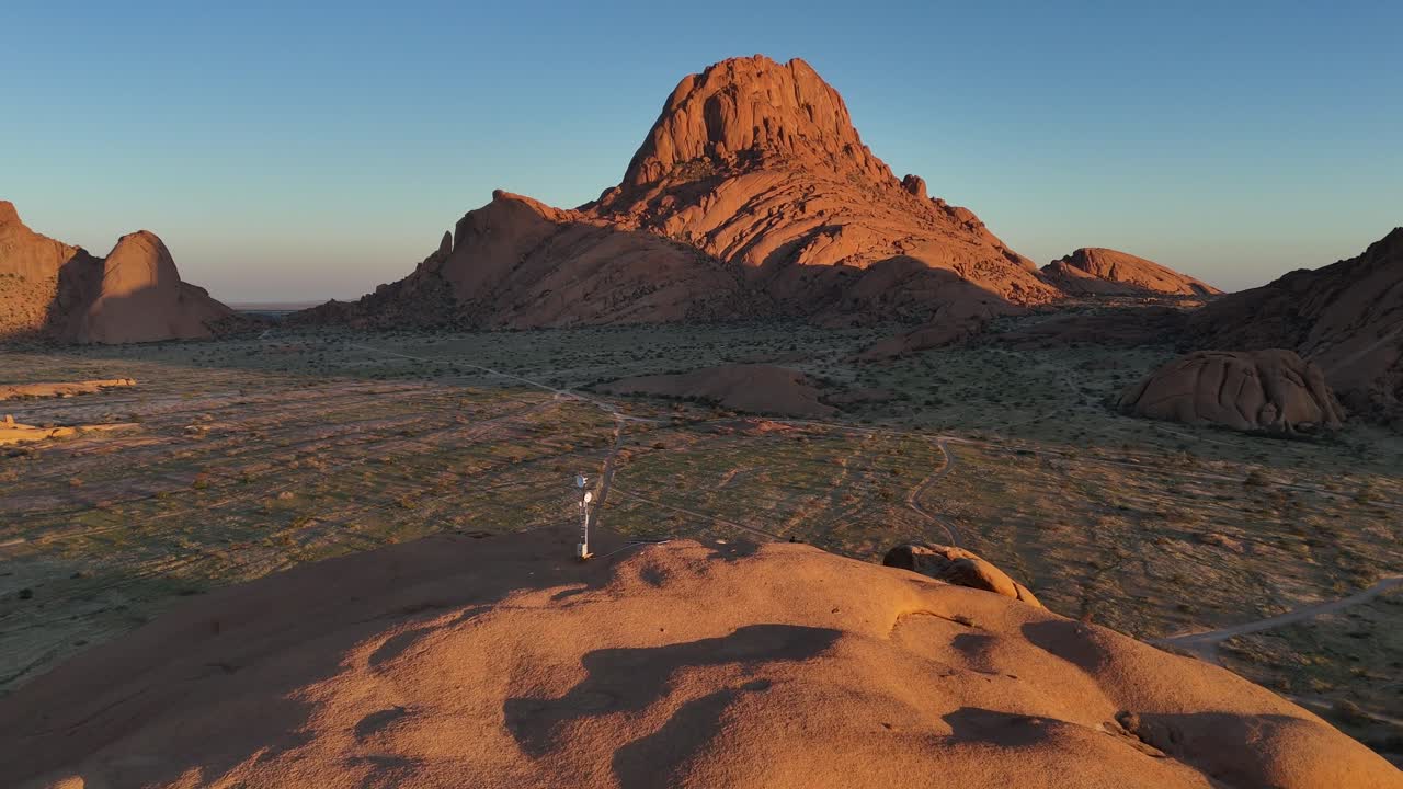 scenic sunset aerial view of massive red granite boulders at Spitzkoppe, surrounded by dry savanna vegetation and the open Namibian desert under clear skies