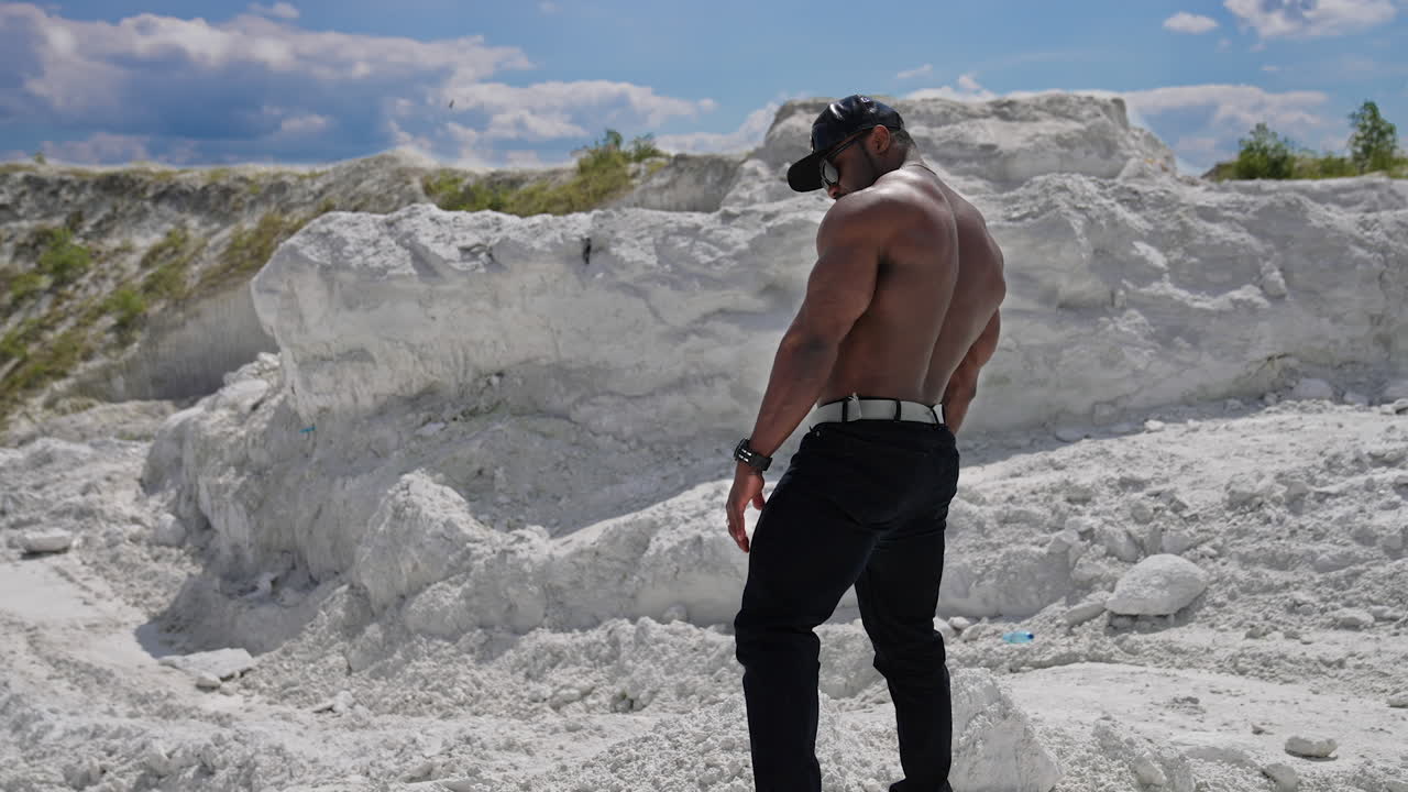 Motion camera view of the athletic young shirtless bodybuilder with naked torso posing for camera and showing his body