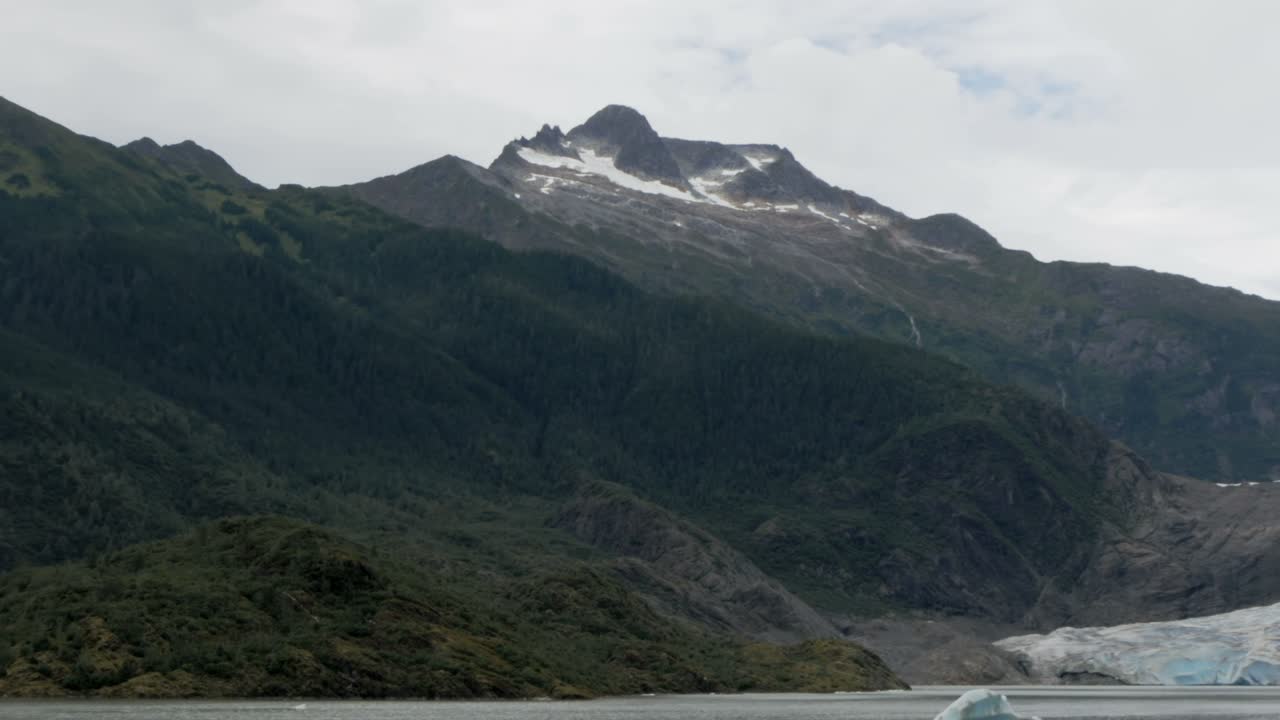 거대한 빙하는 바위와 녹색 알래스카 산맥 사이에 있으며 주노의 알래스카 피요르드 내에 있습니다.