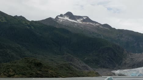 un enorme glaciar se encuentra entre una cordillera rocosa y verde de alaska, dentro de un fiordo de alaska en juneau