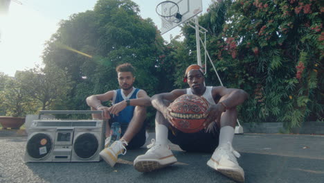 two basketball friends sitting with ghetto blaster and ball on playground