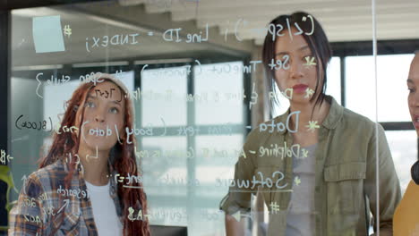 diverse female team collaborating on coding project, writing on glass board in modern office