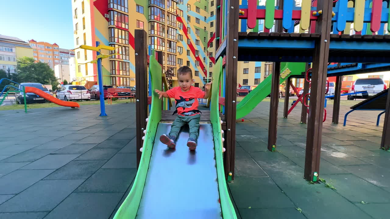 Beautiful baby boy climbs the slide on the playground. Active kid slides down and runs away.
