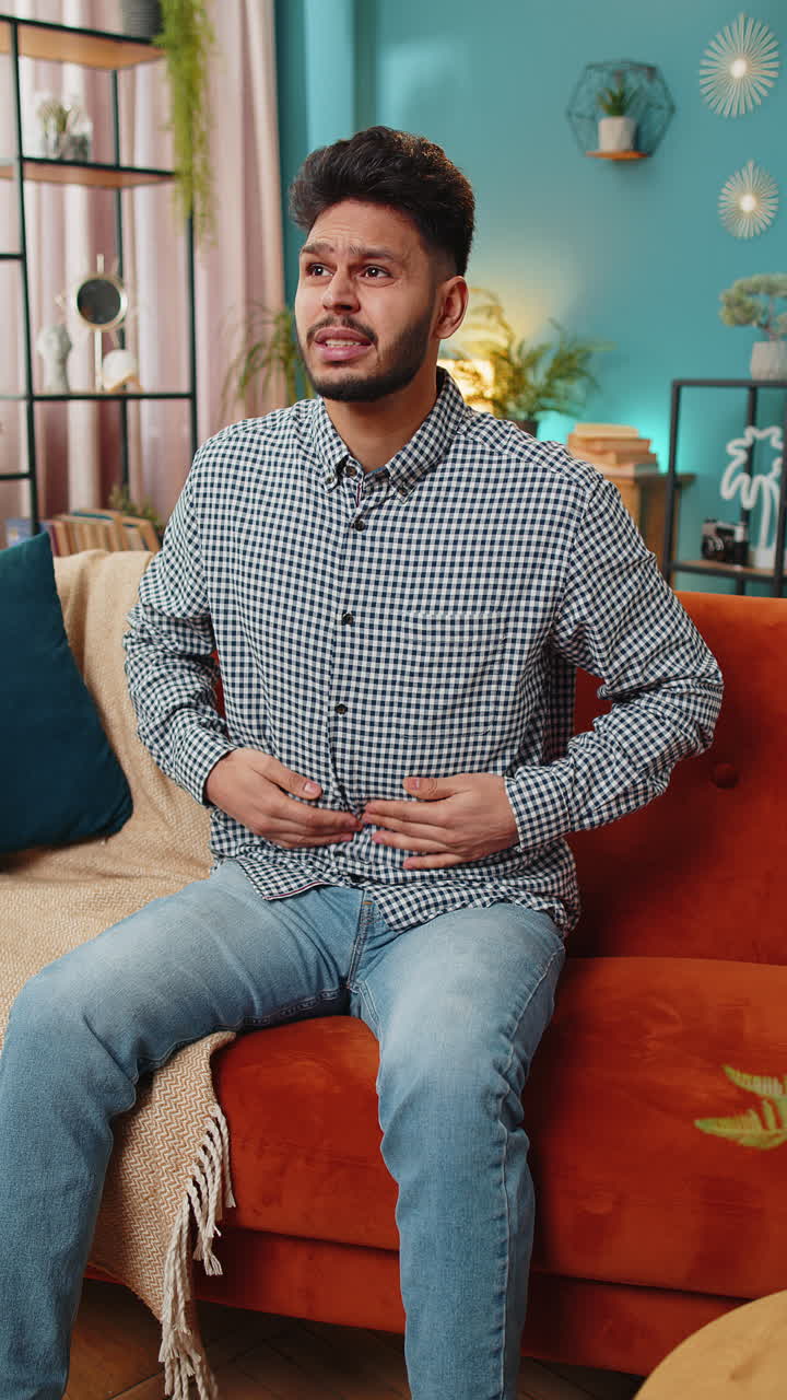 Arabian man sits on sofa feeling sudden strong abdominal stomach ache gastritis problem diarrhea