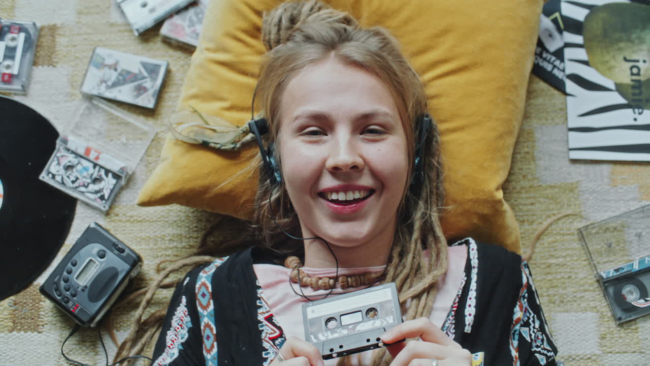 Ritratto di una ragazza allegra con le cuffie che tiene una musicassetta e sorride