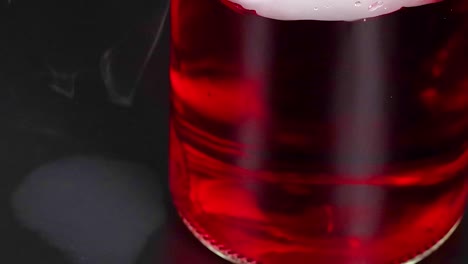 un vaso con líquido rojo reacciona con hielo seco, creando niebla y burbujas en un entorno oscuro