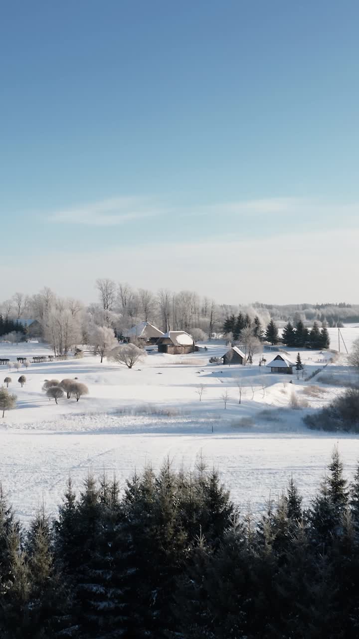 Scenic vertical aerial drone view of a cozy country house in a sunny snow-covered winter morning. Lifestyle of living in countryside. Clean environment.