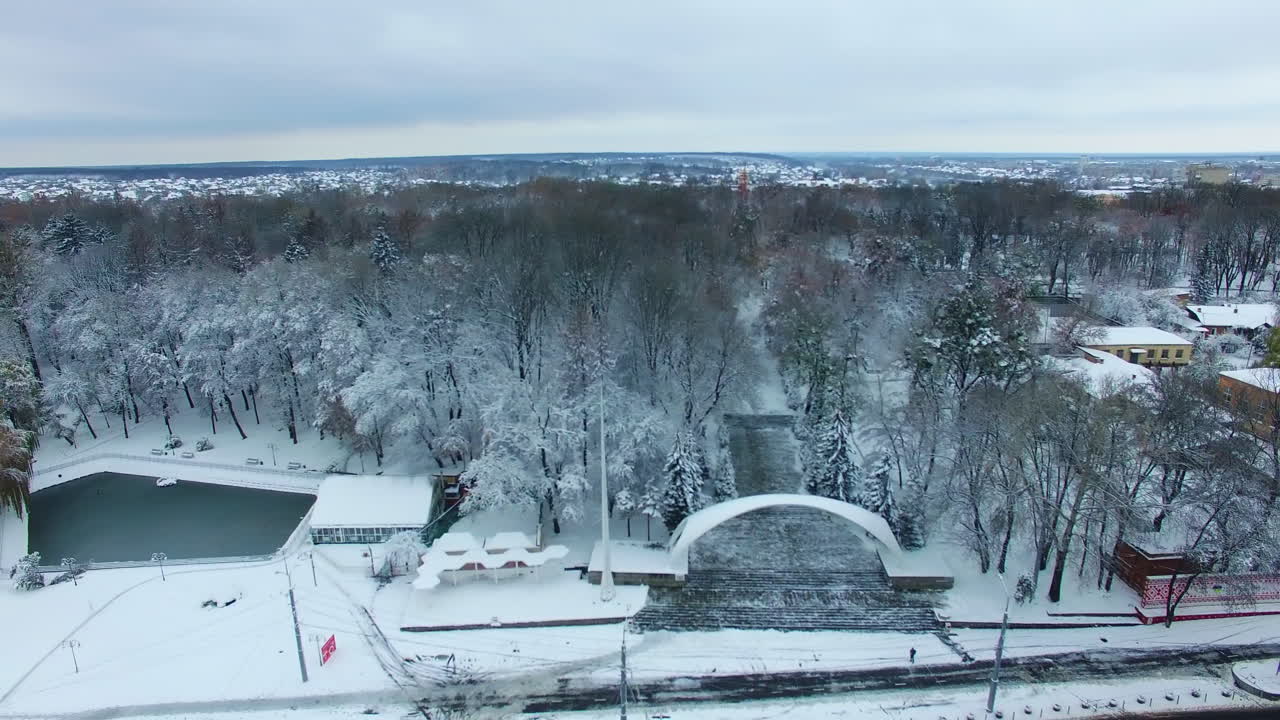 Central entrance with the arch to the city park. Trees in snow and city panorama from aerial view.