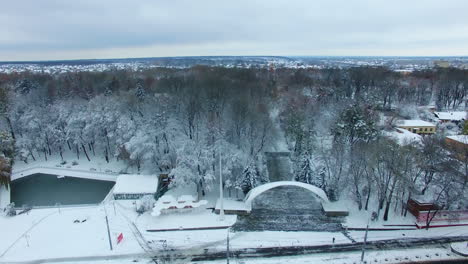 central entrance with the arch to the city park. trees in snow and city panorama from aerial view.
