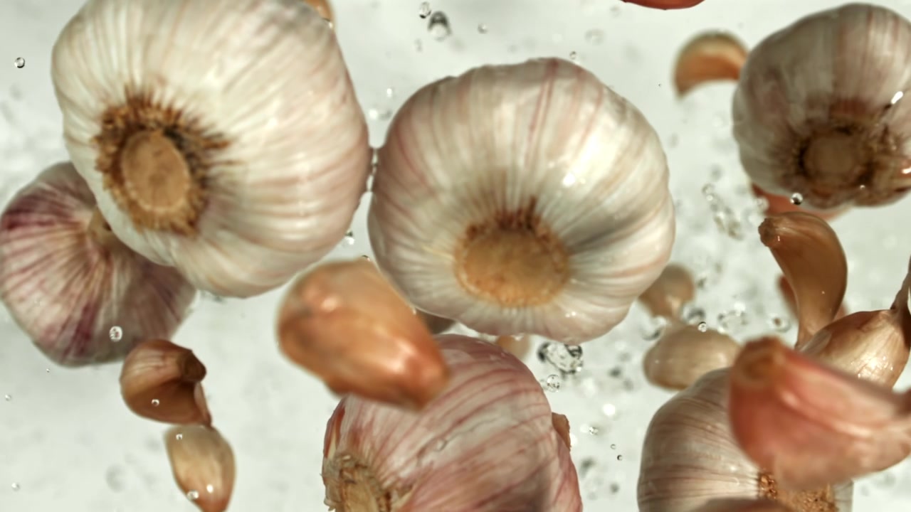 Aglio fresco e spicchi che galleggiano nell'acqua con schizzi al rallentatore