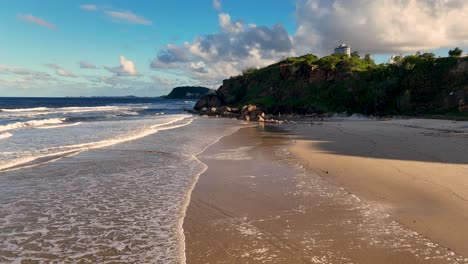 a serene view of waves rolling onto burleigh beach, gold coast, under a clear blue sky with scattered clouds