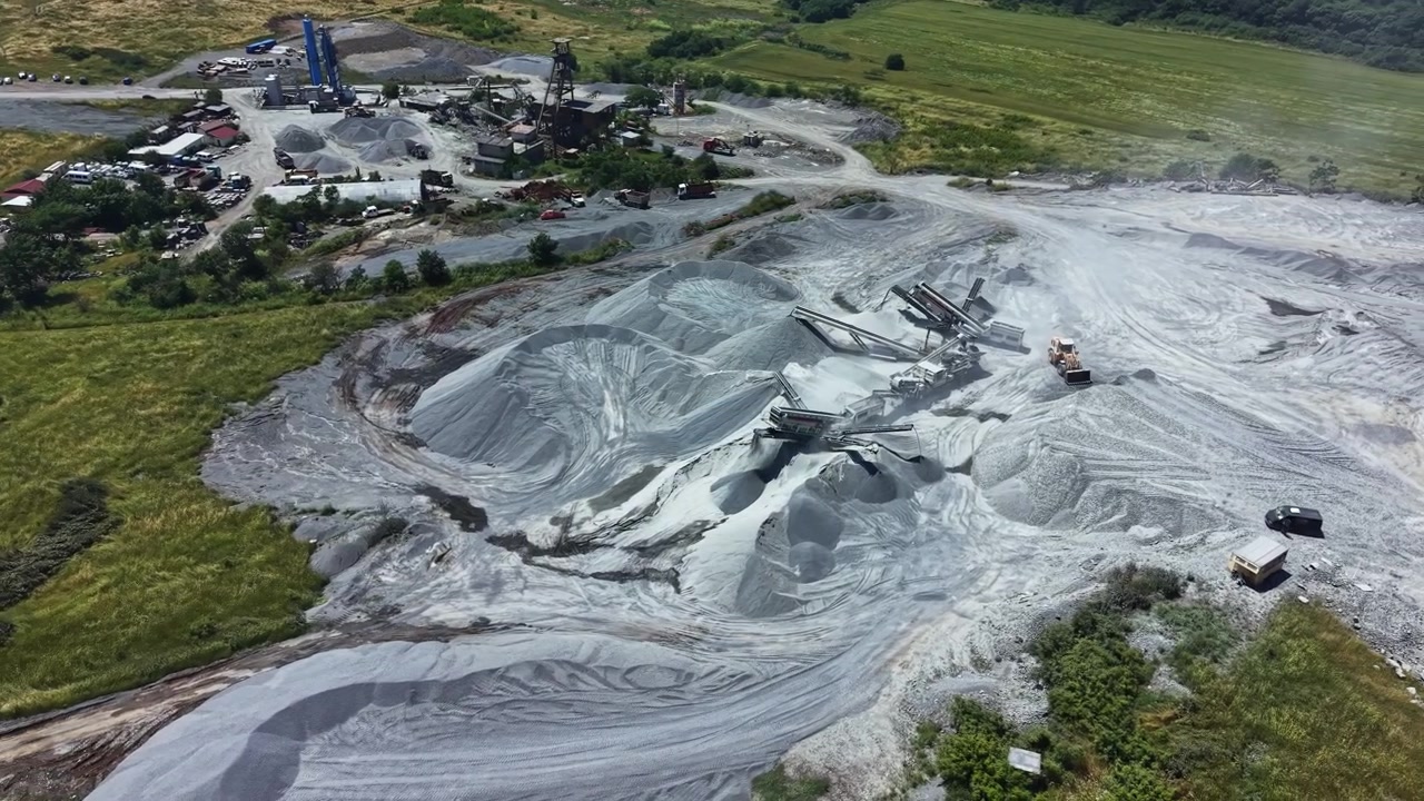 Granite quarry operations on a sunny day in a rural area with workers and machinery moving materials and extracting granite resources