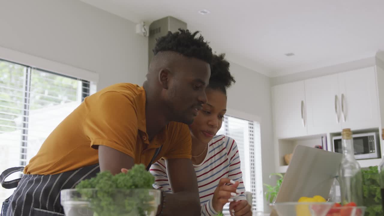 Vidéo d'un joyeux couple afro-américain cuisinant ensemble dans la cuisine avec une tablette