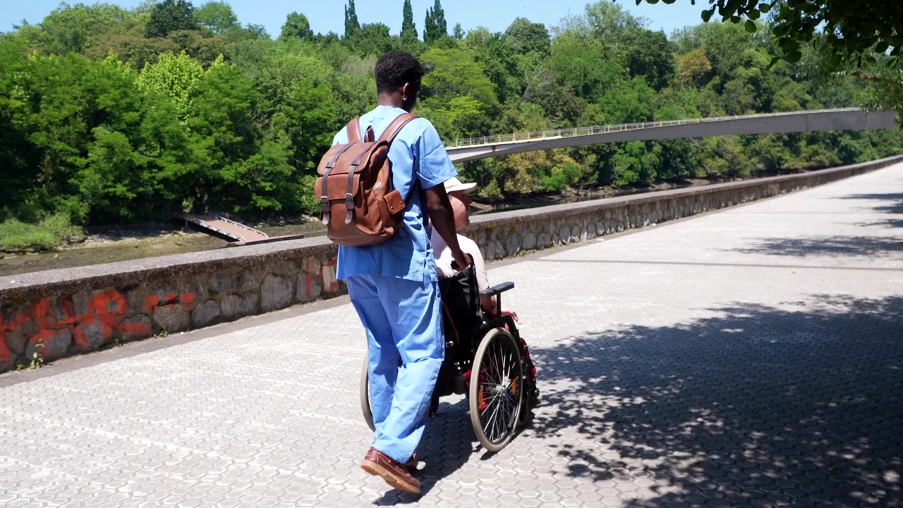 Caregiver Pushing Senior Patient in Wheelchair Along Sunny Park Path