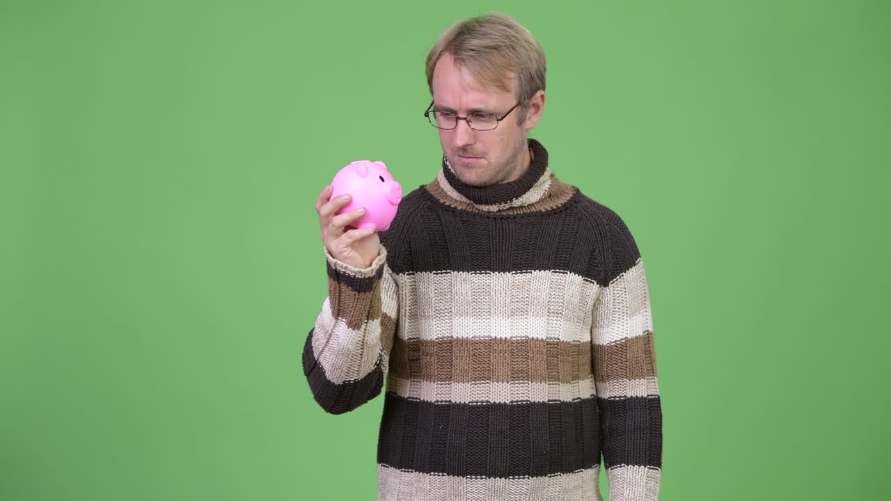 금발의 잘생긴 남자가 돼지 은행을 들고 겨울을 준비하고 있습니다.
