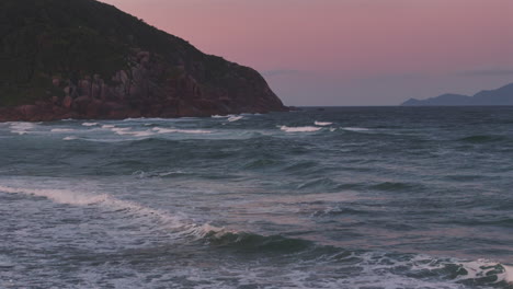 waves crashing on praia brava with a rocky mountain backdrop during a breathtaking sunset