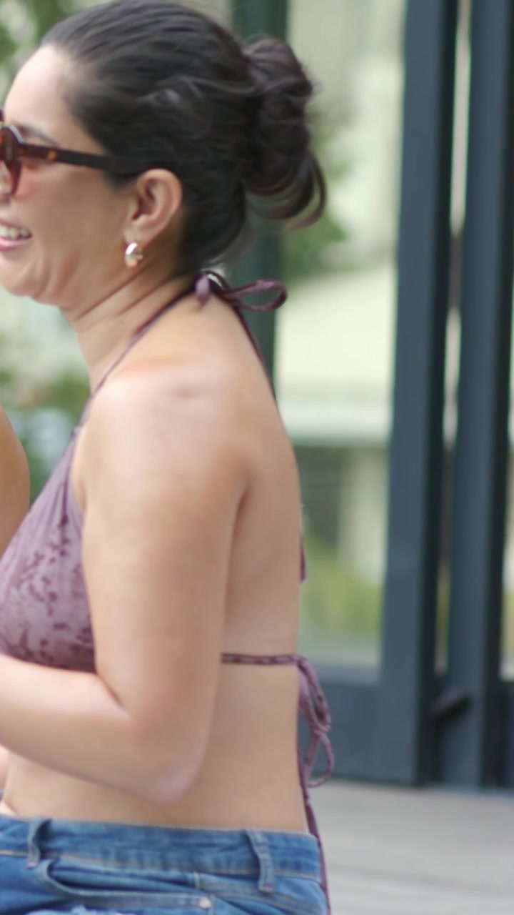 Video verticale: Donna sorridente che si gira verso una voce fuori campo su un patio, indossando un top all'americana e jeans.
