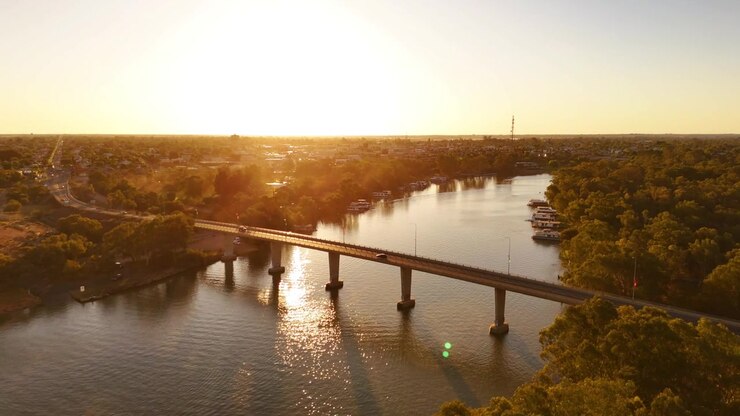 Ponte di Mildura che si estende sul fiume Murray con il caldo bagliore del tramonto e l'acqua tranquilla che scorre sotto, ripresa aerea orbitale