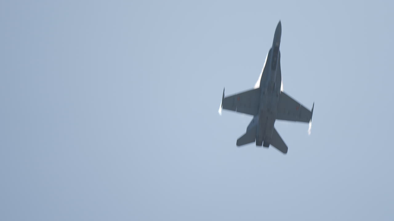 Military jet aircraft flying fast above with visible aerodynamic condensation as it passes overhead
