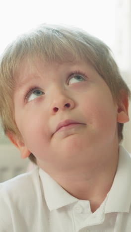 dreaming little boy looks up solving tasks at desk in home classroom closeup. funny toddler pupil thinks of homework preparing for future school lessons