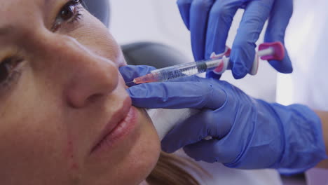 mujer madura sentada en una silla recibiendo una inyección de botox por una doctora